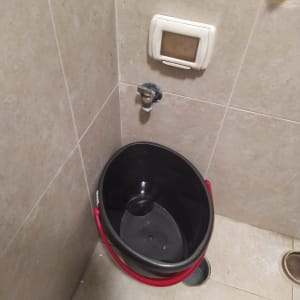 דלי שחור עם ידית אדומה ליד ברז קיר