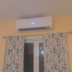 מזגן מותקן על קיר מעל חלון עם וילונות צבעוניים