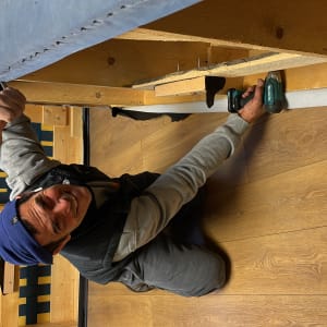 אדם מחזיק מברגה מתחת לספה מעץ