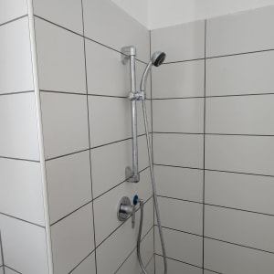 ראש מקלחת מותקן על קיר אריחים לבנים