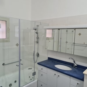 חדר אמבטיה עם מקלחון זכוכית, כיור וברז מודרני.