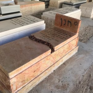 מצבות עם כיתוב בעברית ואבנים קטנות מונחות עליהן