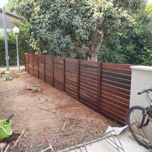 גדר עץ חומה בגינה עם אופניים ודלי ירוק