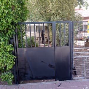 שער מתכת שחור עם סורגים, עץ ברקע