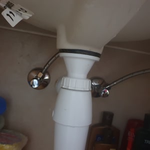 צינור פלסטיק לבן עם חיבורים מתכתיים מתחת לכיור