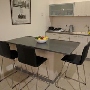 מטבח מודרני עם אי, כיסאות שחורים וקערת פירות על השולחן