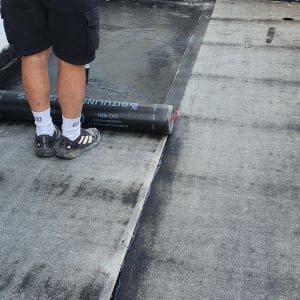 אדם מיישם יריעות ביטומניות לאיטום גג