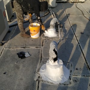 אדם מורח חומר איטום לבן על צינור בגג