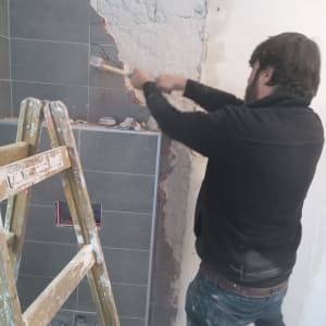 אדם מפרק קיר עם פטיש ליד סולם עץ