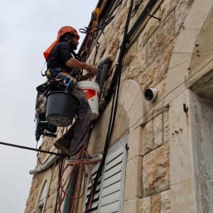 אדם עם קסדה עובד על צינור מים על קיר אבן