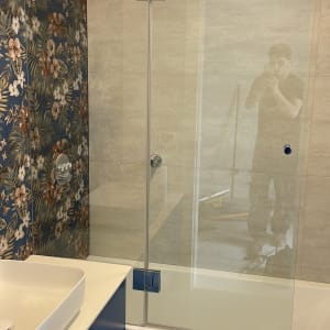 מקלחת עם דלת זכוכית וברז מתכת על קיר פרחוני