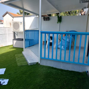 דשא סינתטי, מרפסת עם מעקה כחול, כלי עבודה וניירות על הקרקע