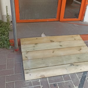 רמפת עץ על מדרכה ליד דלת כתומה
