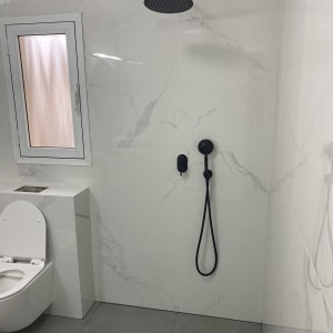 מקלחת עם ראש גשם שחור וקיר שיש לבן