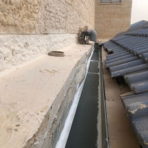 מרזב גג עם רעפים כחולים וקיר אבן