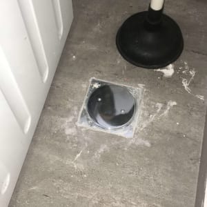 פומפה שחורה על רצפה ליד מכסה ניקוז מתכת