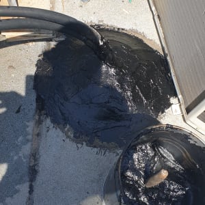 חומר איטום שחור נמרח על גג ליד צינורות