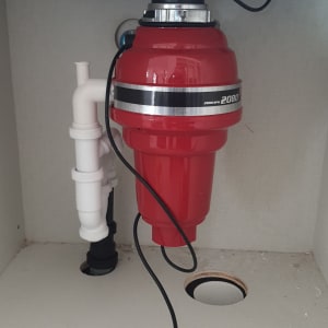 מטחנת אשפה אדומה מותקנת מתחת לכיור עם צינור לבן