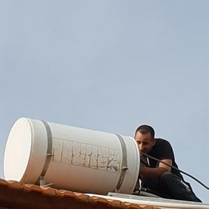 אדם מתקין דוד שמש על גג רעפים