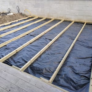 קורות עץ מונחות על יריעת פלסטיק בגינה