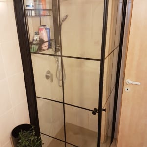 מקלחון זכוכית עם ראש מקלחת ומדף מוצרי טיפוח