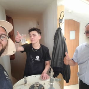 שלושה אנשים ליד דוד שמש עם צינור ומד מים