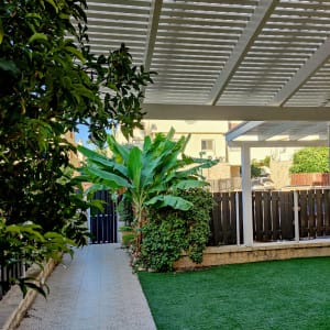 פרגולה לבנה מעל דשא סינתטי ושביל מרוצף