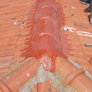 אדם צובע גג רעפים בצבע אדום עם מברשת