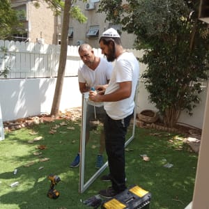 שני אנשים מתקנים תריסים עם כלים בחצר