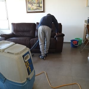 אדם מנקה ספה עם מכונת ניקוי מקצועית