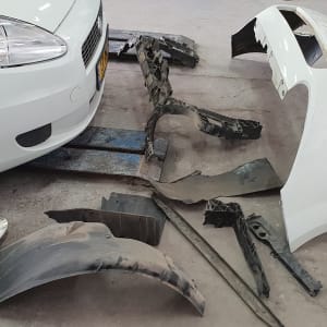 חלקי רכב מפורקים ליד רכב לבן במוסך