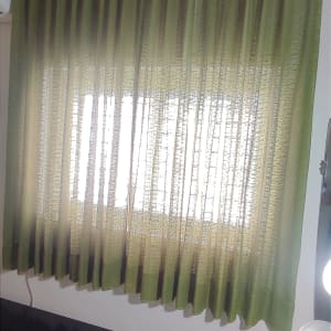 Green curtain hanging over a window with light filtering through.