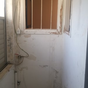 קיר מתקלף עם דלי צבע שחור על הרצפה