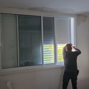 אדם מתקין תריסי אלומיניום בחלון גדול