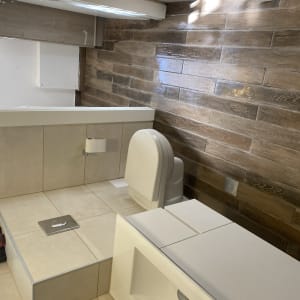 שירותים עם רצפת עץ, קיר אריחים, ומיכל ניקוי