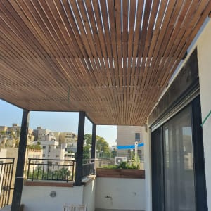 פרגולה מעץ מעל מרפסת עם שולחן וכיסאות