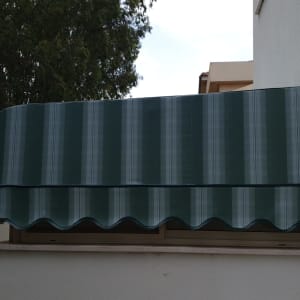 סוכך ירוק מפוספס מותקן מעל חלון קיר חיצוני