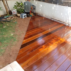 אדם מתקין דק עץ בגינה ליד קיר וגדר.