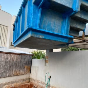 מכולה כחולה תלויה מעל חפירה באתר שיפוצים