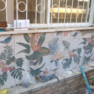 עובד מתקין אריחים עם דוגמת צמחים על קיר חיצוני