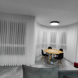 וילונות לבנים תלויים על חלונות גדולים בחדר.