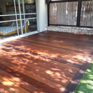 דק עץ חום ליד דשא סינטטי וגדר במבוק