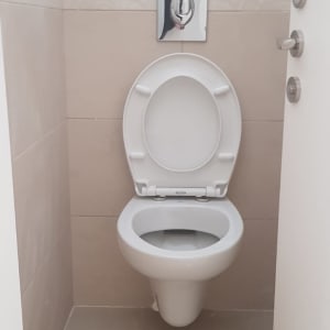 אסלה לבנה עם לחצן הדחה על קיר אריחים