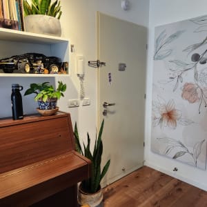 A room with a piano, plants, and a floral painting on the wall.