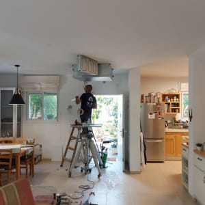 אדם מתקין מזגן בתקרה על סולם