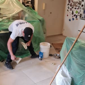 אדם משפץ רצפה עם דלי, מטאטא ושק מלט
