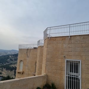 קיר אבן עם גדר מתכת לבנה וחוט חשמל חשוף