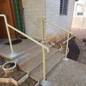 מעקה מתכת צהוב ליד מדרגות כניסה לבית