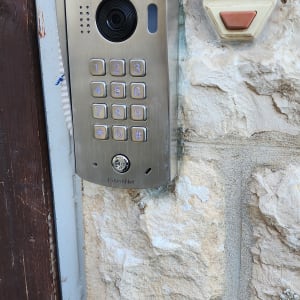 אינטרקום מתכתי עם מצלמה ולוח מקשים על קיר אבן