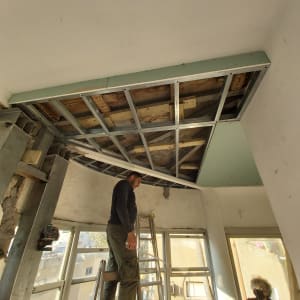 בעל מקצוע מתקין תקרת גבס מונמכת על קונסטרוקציית מתכת במהלך שיפוץ